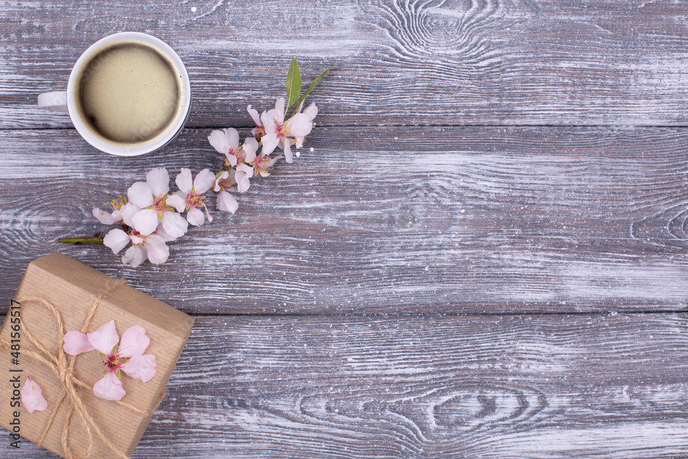 Spring composition with coffee, a gift wrapped in craft paper, spring blossoming almond branches with flowers on a gray shabby wooden table. Flat lay, copy space Spring composition with coffee, a gift wrapped in craft paper, spring blossoming almond branches with flowers on a gray shabby wooden table. Flat lay, copy space