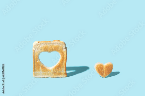 Love concept. Minimal arrangement made of slice of toasted bread with a heart shape inside of it and little heart shaped toast beside it. Bright blue background