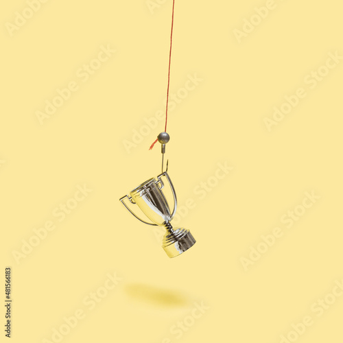 Minimal concept out of hook. Arrangement made of shiny trophy on a fish hook. Pastel yellow background.