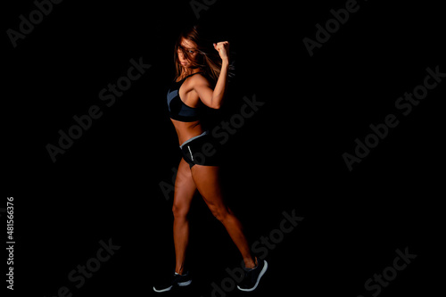 Beautiful athletic woman showing muscles on dark background. Slim tanned woman's body over black wall.