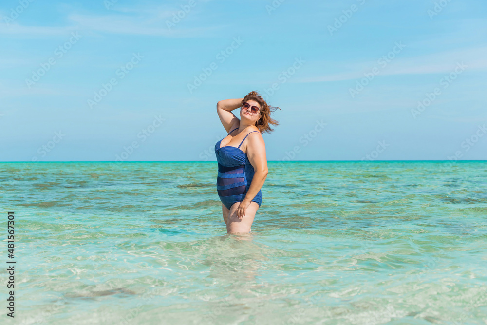 Body positive concept. Middle age lady at the beach in blue swimsuit resting and have a nice time Body positive concept. Middle age lady at the beach in blue swimsuit resting and have a nice time