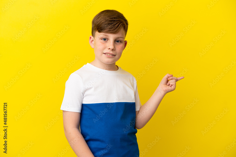 Little redhead boy isolated on yellow background pointing finger to the side Little redhead boy isolated on yellow background pointing finger to the side