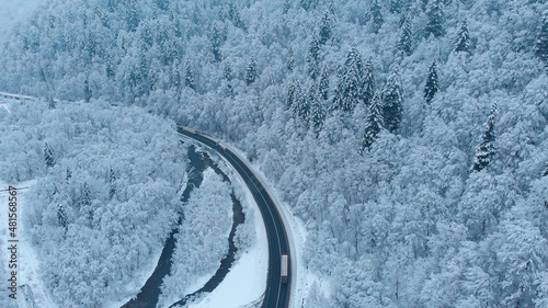 Aerial shot: Trucks driving by the road in winter forest. © Motionstocks