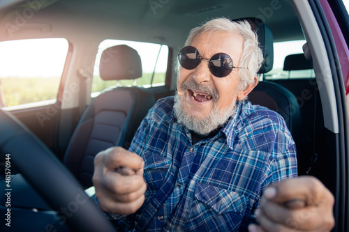 Happy senior man pensioner in round sunglasses smiling and driving car