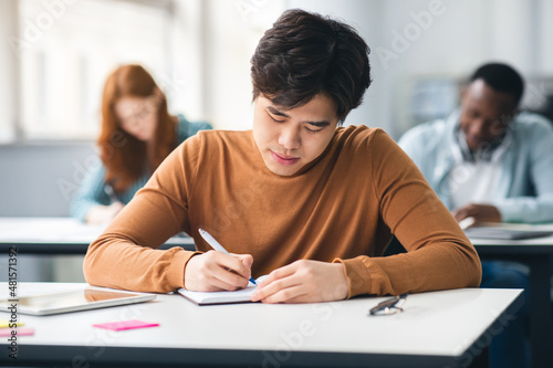 Asian student sitting at desk in classroom writing in notebook