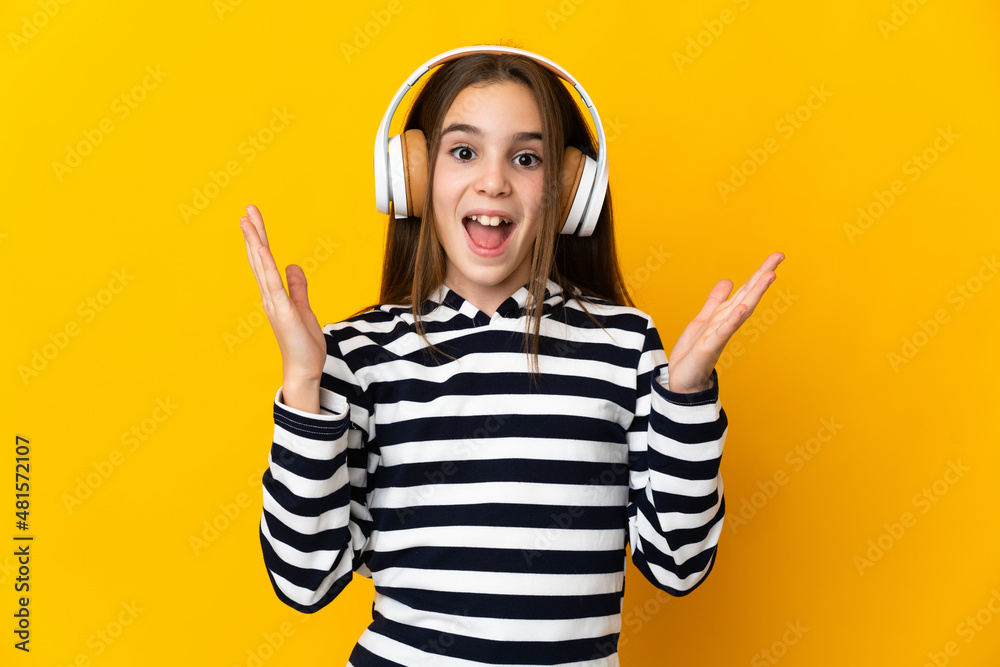 Little girl isolated on yellow background surprised and listening music Little girl isolated on yellow background surprised and listening music