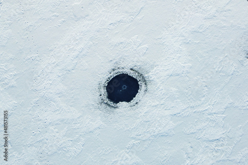 Aerial view of a dark ice hole on the surface of a frozen lake in winter