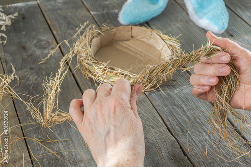Handmade master class Easter nest made of natural dry grass and used cardboard. The hands of an elderly woman show step by step how to make an Easter nest on wood background