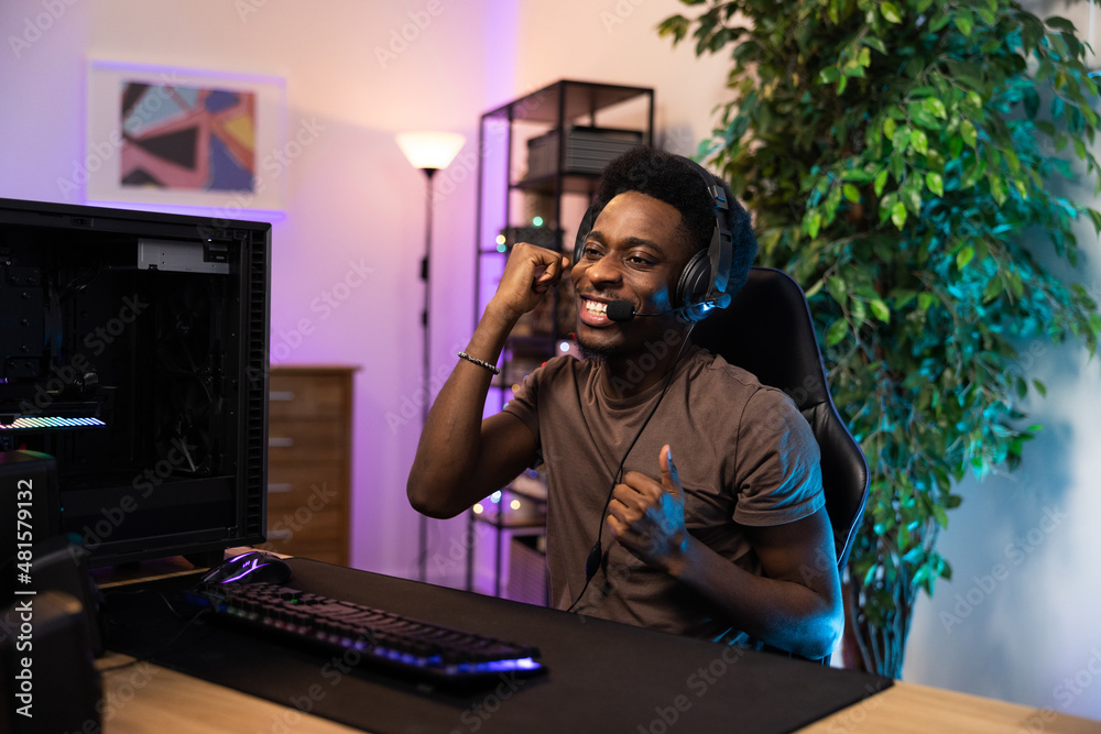 Handsome Pro Gamer man streaming online video game winning it raises hands up as a sign of victory wearing a headset sharing with fans of the team fun, background neon retro led colors Handsome Pro Gamer man streaming online video game winning it raises hands up as a sign of victory wearing a headset sharing with fans of the team fun, background neon retro led colors