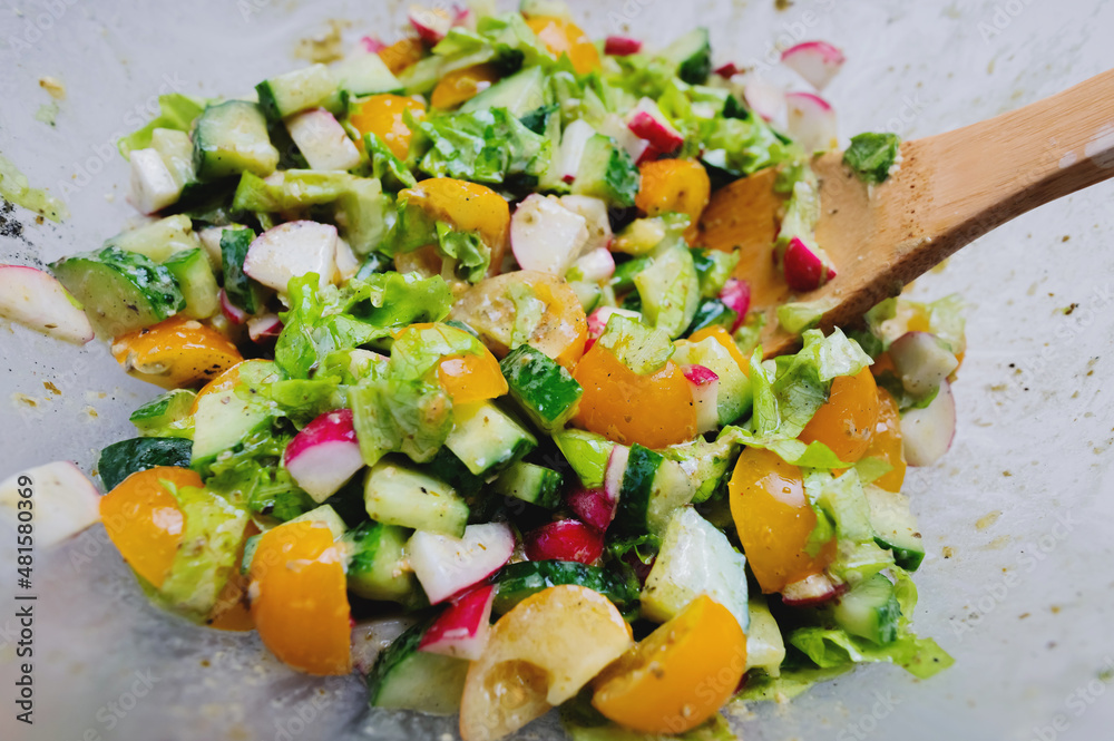 Close-up of a fresh vegan salad of fresh and tasty vegetables in a transparent bowl with a wooden spoon. Detox salad bowl view Close-up of a fresh vegan salad of fresh and tasty vegetables in a transparent bowl with a wooden spoon. Detox salad bowl view
