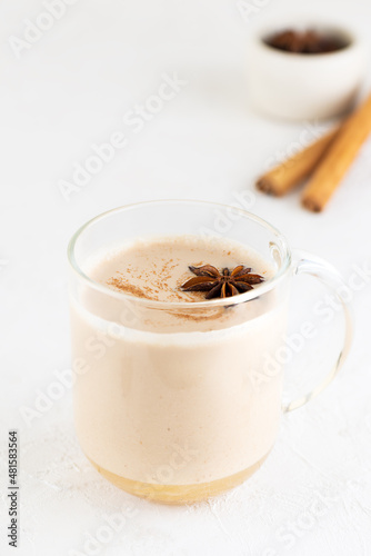 Masala tea with milk and spices in a glass mug on the table.
