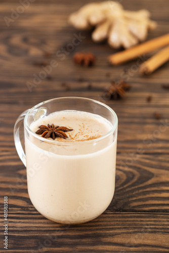 Indian homemade masala chai with milk and spices in a glass mug on a wooden table. Lactose free, vegan.