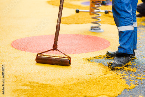 Worker leveling and pressing rubber coating for playgrounds with roller, mason hand spreading soft rubber crumbs. Outdoor soft coating and floor covering for sports. Selective focus. photo