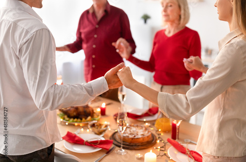 Closeup of young family celebrating Thanksgiving or Christmas with senior parents  praying before festive dinner at home