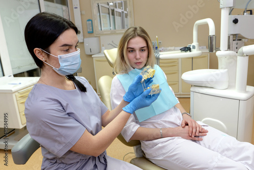  attractive dentist in latex gloves holding teeth model near patient with clenched hands