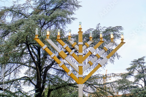 Hanukkah menorah, hanukkiah, nine-branched candelabrum lit during. Jewish holiday of Hanukkah. Hanukkah symbol on the street of the city across the sky and tree