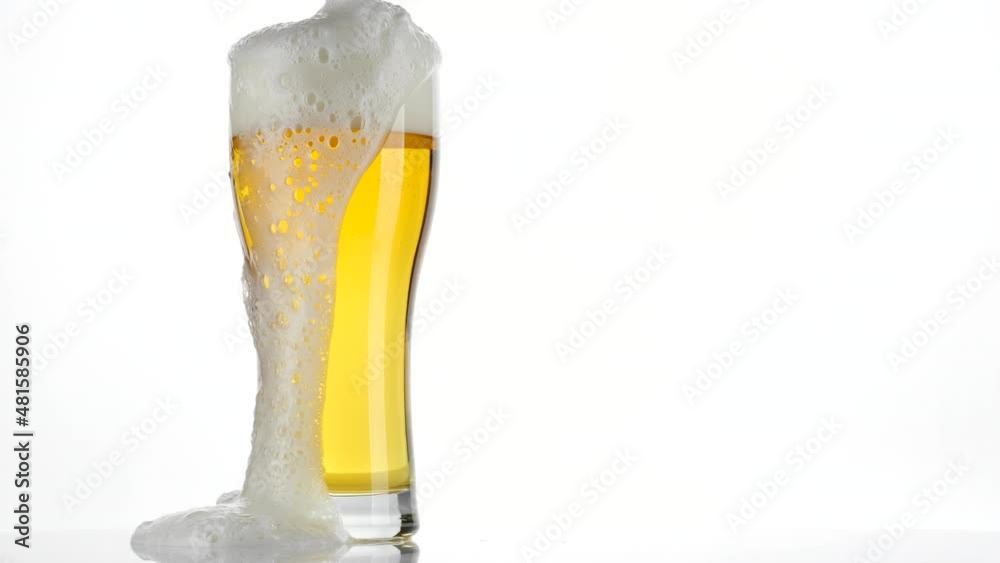 Glass of beer on white background. Foam flows down the glass. 4K UHD video