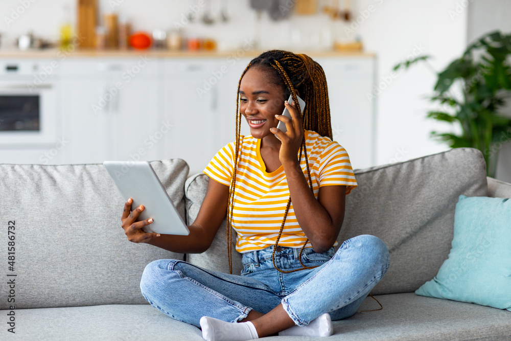 Obraz premium Afro american woman freelancer talking on phone and using tablet