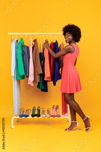 Black Lady Choosing Clothes Enjoying Shopping Over Yellow Background, Vertical
