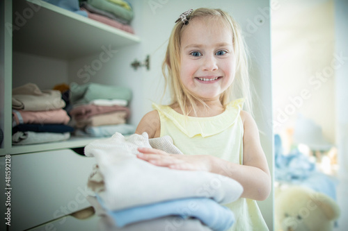 Little caucasian blonde girl neatly folds clothes on her shelf