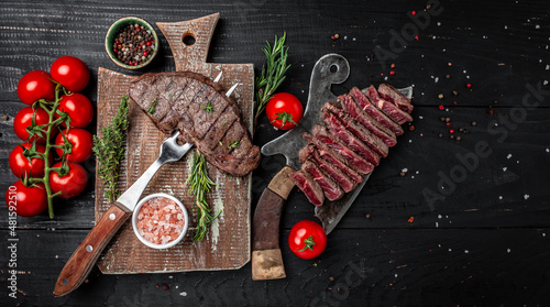 Grilled beef steak on a fork adding rosemary on black background. banner, menu, recipe place for text, top view