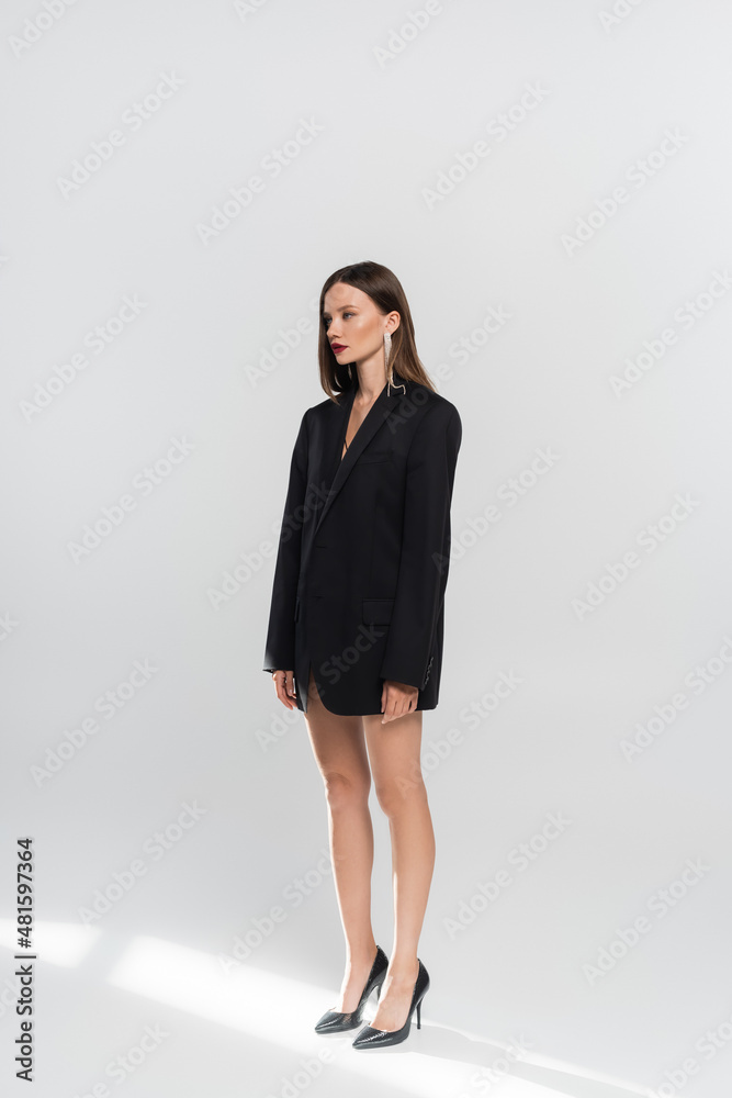 young brunette woman with naked legs, wearing black blazer and high-heeled shoes on grey. young brunette woman with naked legs, wearing black blazer and high-heeled shoes on grey.