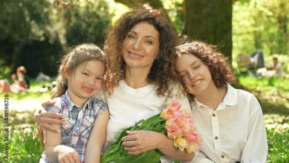 Two girls of different ages hug their mother. The woman is holding a beautiful bouquet of tulips. Against the background of a spring park. Mothers Day. Two girls of different ages hug their mother. The woman is holding a beautiful bouquet of tulips. Against the background of a spring park. Mothers Day.