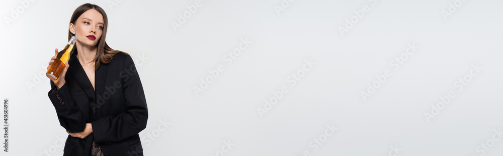 sensual woman in black blazer standing with bottle of beer and looking away isolated on grey, banner. sensual woman in black blazer standing with bottle of beer and looking away isolated on grey, banner.