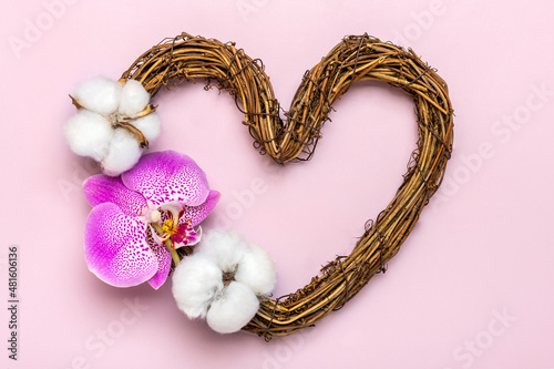 heart shaped rattan wreath decorated with tropical flowers of orchid, cotton on pink background Top view Flat lay Holiday card Happy Valentine's day, love concept Copy space