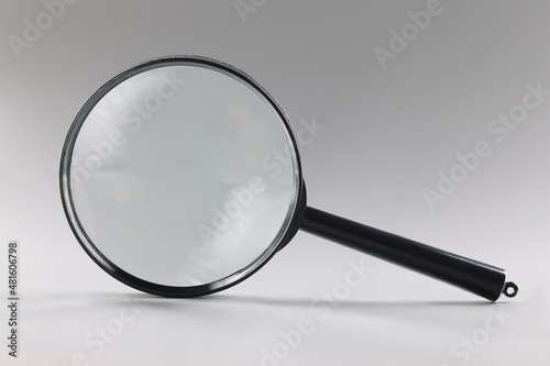 Single magnifying glass with black handle, leaning on grey surface