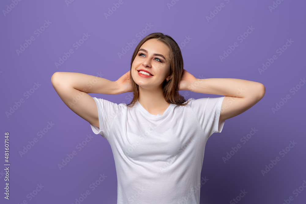 Fototapeta premium Portrait of dreaming brunette girl looking up with pleased face. Young woman relaxing, resting with hands behind head, carefree pose, purple background.