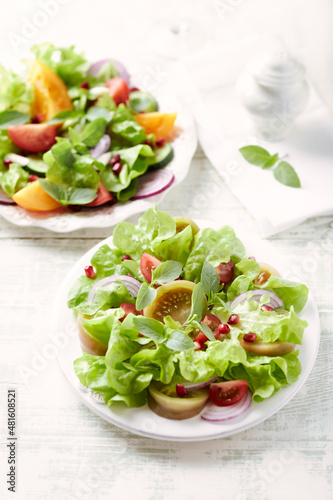 Salad with red and yellow Tomatoes and Pomegranate Seeds on bright wooden Background. Close up.