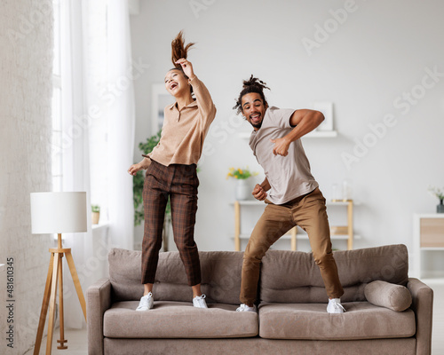 Young overjoyed african american family couple dancing to music on sofa at home
