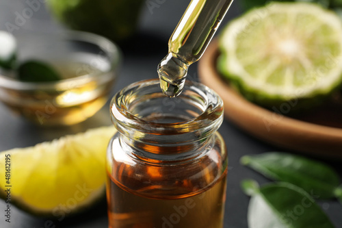 Bergamot essential oil dripping from pipette into bottle on table, closeup photo