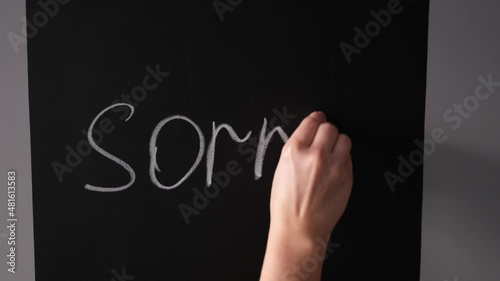 girl writes on a chalk board with chalk the word sorry