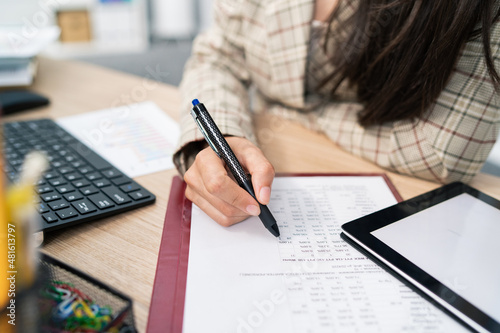 Close-up on a document, statistical table, company's calculations, an office accountant sits at the desk filling in the right places, checking the correctness, touches the paper with a pen