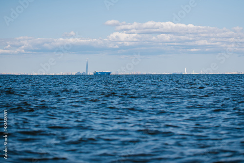 A view from the water of the Gulf of Finland on a summer day, cargo ships and ships are sailing in the distance, blue water and big waves.The coastline of St. Petersburg.Russia, Peterhof, 31.07.2021.