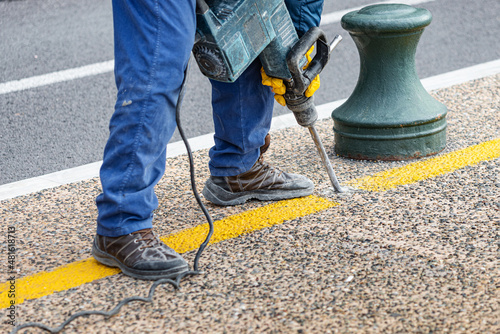 Worker removes the old layer of pavement on a city street with a handheld pneumatic jackhammer. Dangerous road construction work and decibel rumbling photo