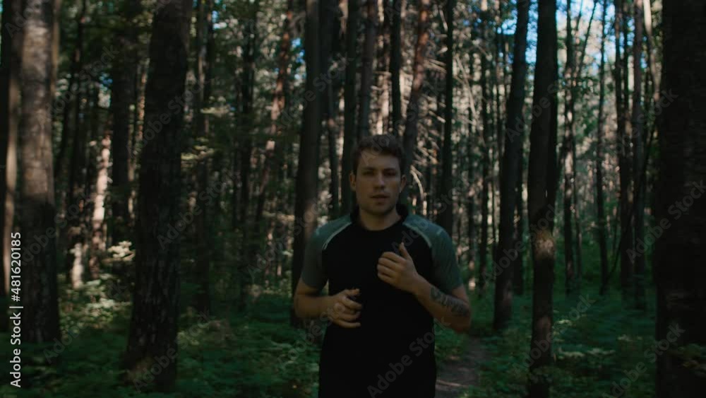 Young athletic handsome man jog through summer forest. Sporty and fit man on morning run in park. Self training application plan on phone, to stay fit and in shape Young athletic handsome man jog through summer forest. Sporty and fit man on morning run in park. Self training application plan on phone, to stay fit and in shape