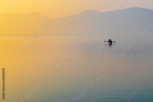 Sunrise time at lake or river with small kayak boat with mountain on the background.
