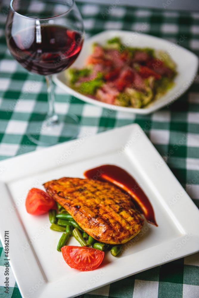 Grilled chicken breast with cherry tomatoes, green French beans, garlic, herbs, served on a white plate Grilled chicken breast with cherry tomatoes, green French beans, garlic, herbs, served on a white plate