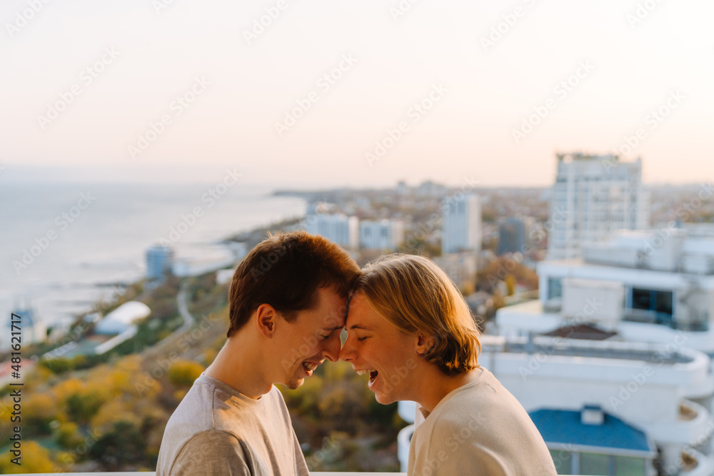 European gay couple laughing while standing head to head on balcony