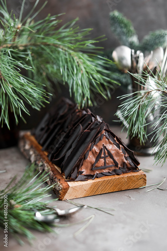 Chocolate cake with chocolate cream and glaze decorations on a wooden board. Sweet treats on a table with pine branches