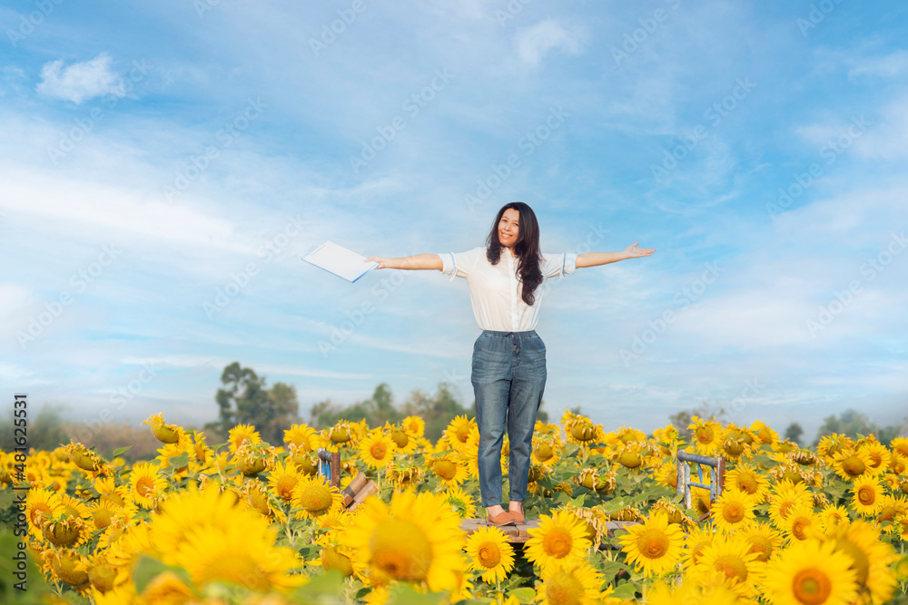 Asian woman farmer proud, excited and victory face, open her arms while holding clipboard and standing in Beautiful summer day over sunflower field. Harvesting, organic farming concept. Asian woman farmer proud, excited and victory face, open her arms while holding clipboard and standing in Beautiful summer day over sunflower field. Harvesting, organic farming concept.