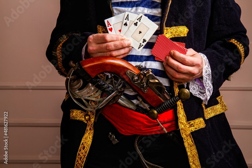 A brave armed pirate captain in a frock coat and a vest with a sword and a dagger plays cards and wins close-up