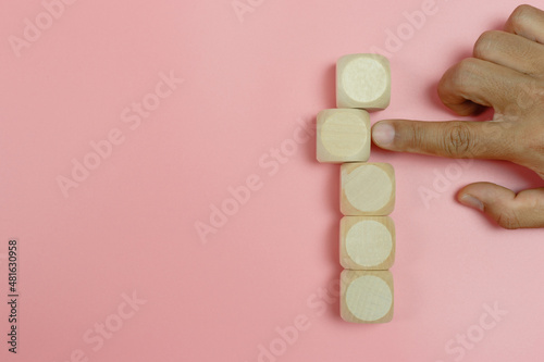 hand finger pointing empty wooden cube block on pink background. create education shape symbol simple.