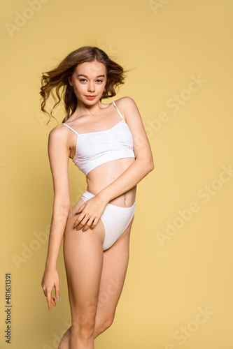 Portrait of young beautiful slim woman in underwear posing isolated over yellow studio background. Natural beauty concept.