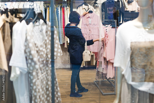 A 40-year-old brunette woman blue jacket is choosing clothes in a store.,