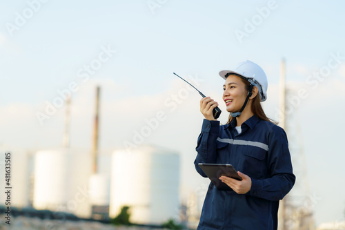 Asian woman technician Industrial engineer using walkie-talkie and holding digital tablet working in oil refinery for building site survey in civil engineering project.