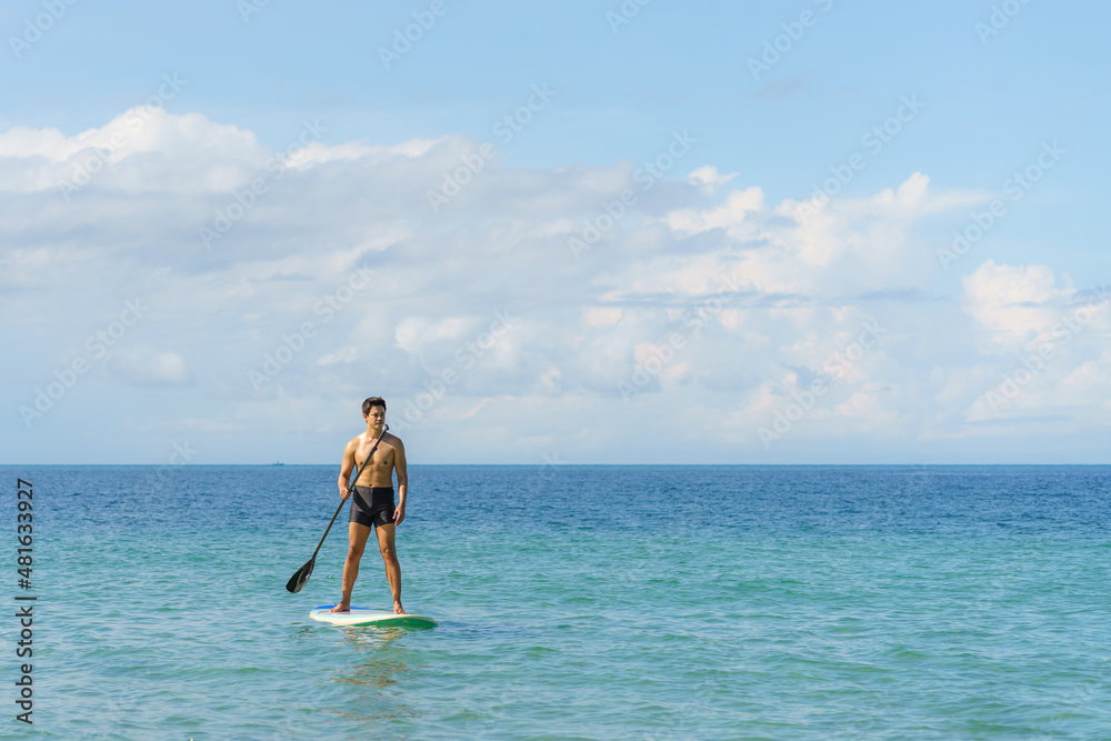 Obraz premium Asian man exercising sup board in turquoise tropical clear waters in summer day..